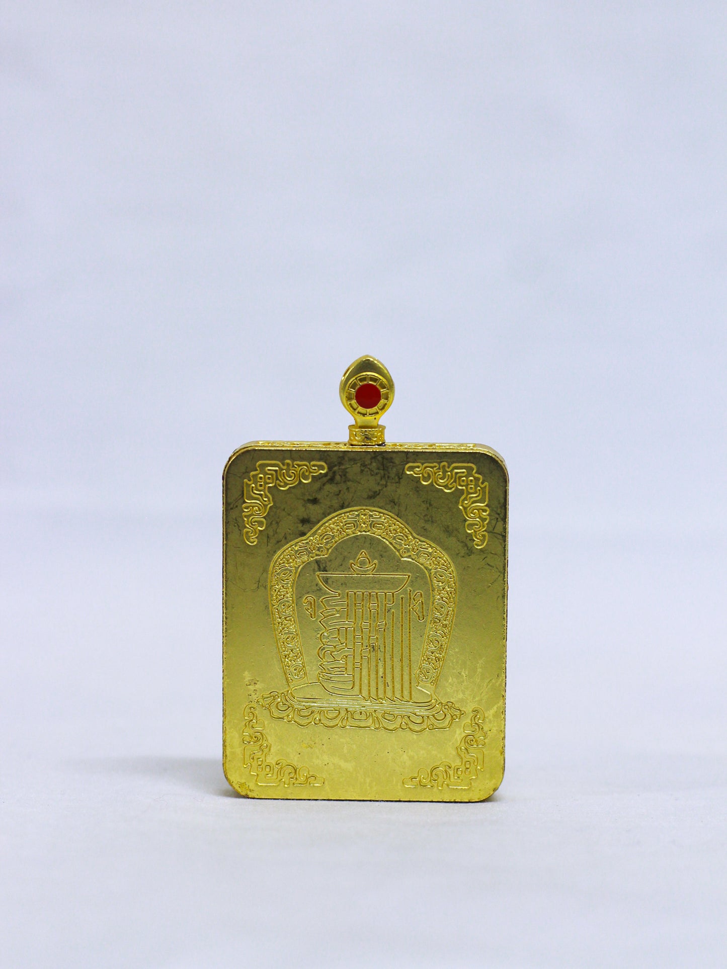 Back of an authentic Green tara thangka locket engraved with the sacred Kalachakra Namchu Wangden emblem, lotus petal, ornate temple arch, floral corner motifs, and a red coral-style stone of the decorative bail