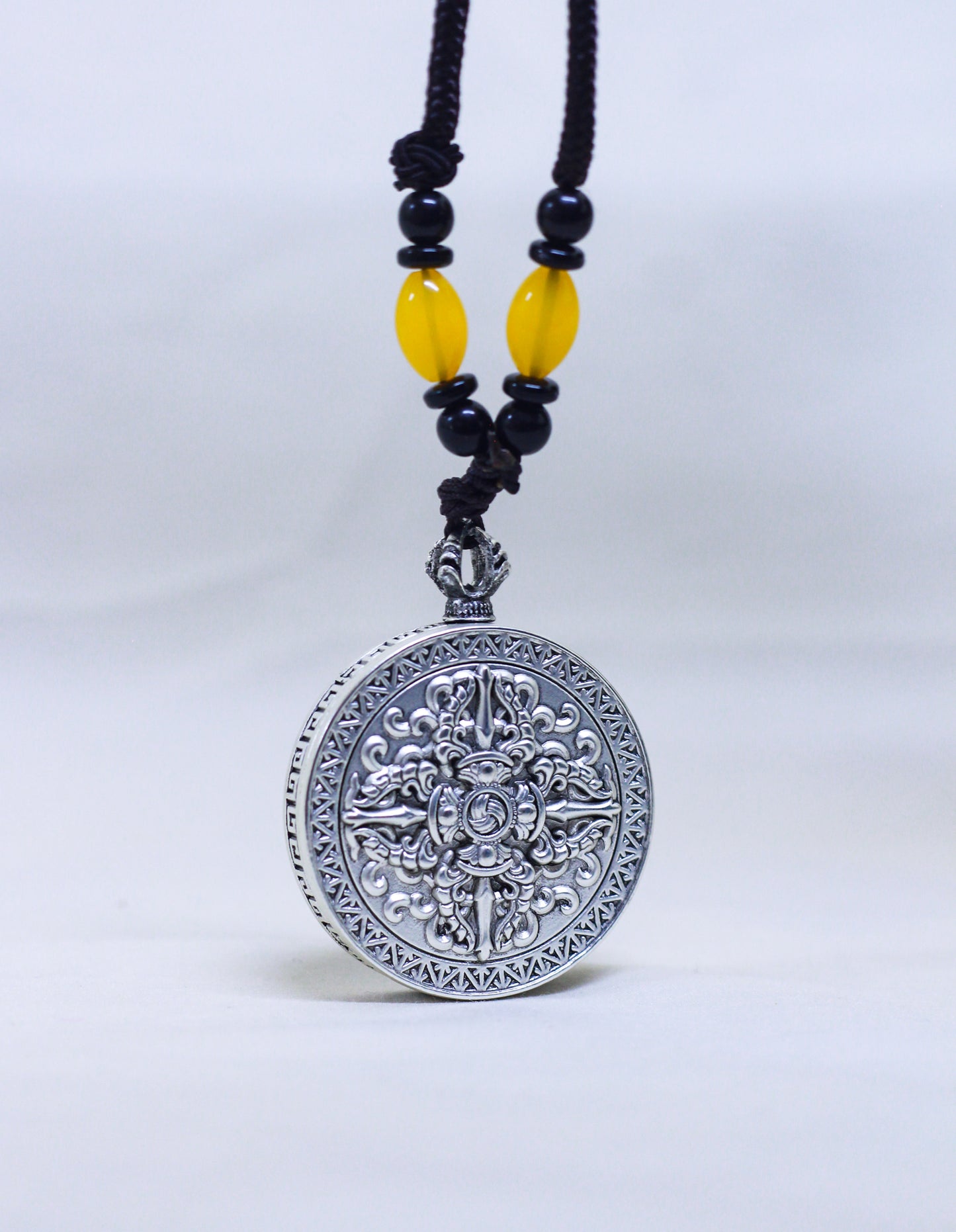 Backside of the silver-toned circular pendant with engraved double vajra and gankyil, a tibetan symbol