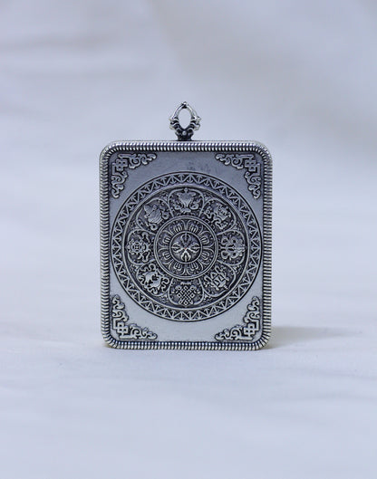 An ornate rectangular silver pendant featuring a detailed circular medallion and decorative border, photographed against a soft white background.