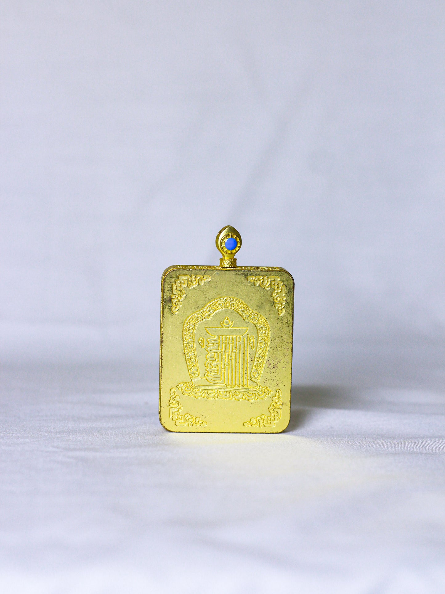 Back side of the golden ghau locket pendant with embossed kalachakra monogram, a sacred symbol in tibetan buddhism, with hoop at the top to tie the chain