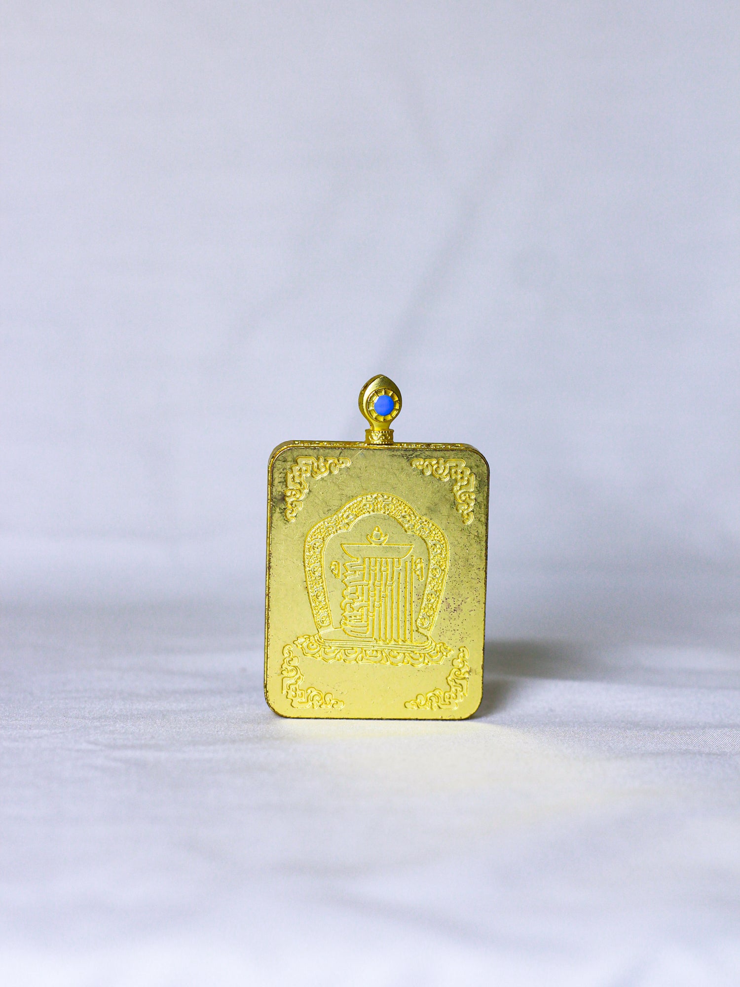 Back side of the golden ghau locket pendant with embossed kalachakra monogram, a sacred symbol in tibetan buddhism, with hoop at the top to tie the chain