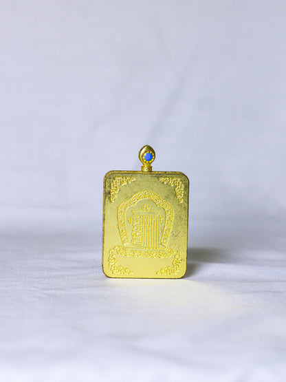 Back side of the golden ghau locket pendant with embossed kalachakra monogram, a sacred symbol in tibetan buddhism, with hoop at the top to tie the chain