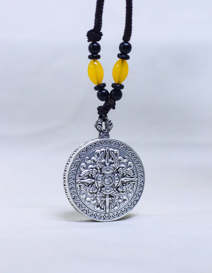 Backside of the silver-toned circular pendant with engraved double vajra and gankyil, a tibetan symbol