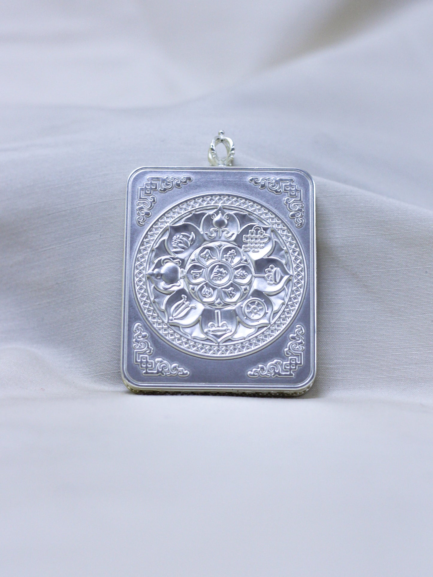 Backside side of ilver-toned pendant with engraved eight-auspicious symbols with decorative corner motifs.