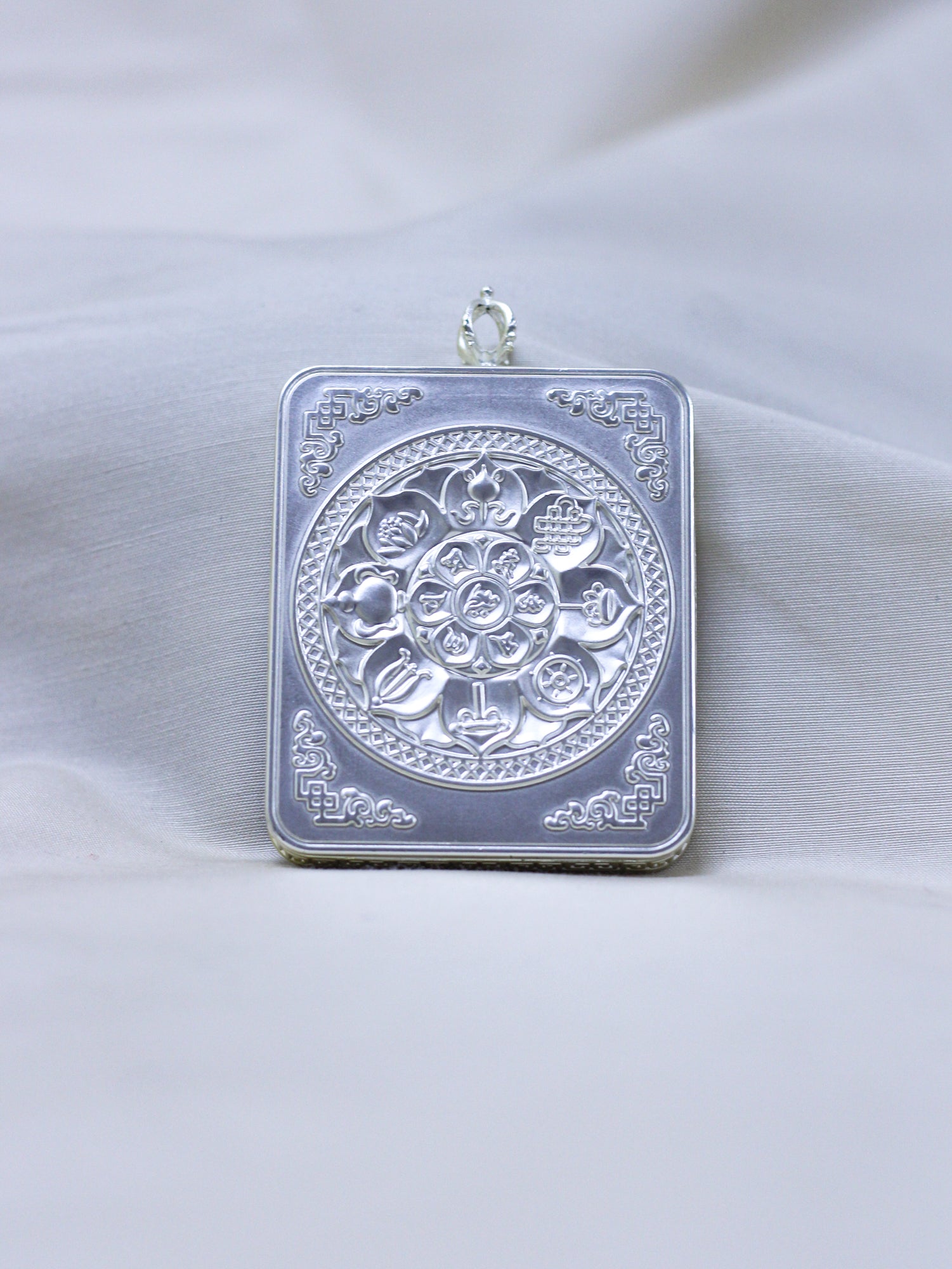 Backside side of ilver-toned pendant with engraved eight-auspicious symbols with decorative corner motifs.