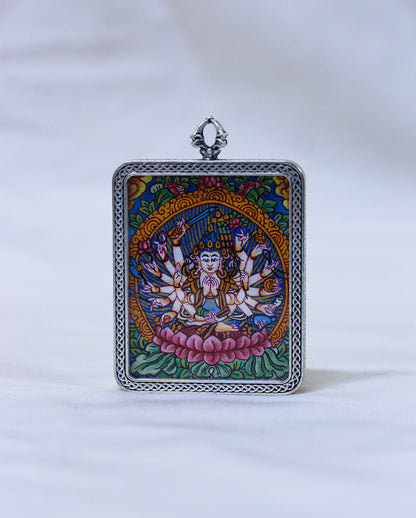 A square silver-toned pendant featuring a colorful Tibetan-style illustration of a multi-armed deity seated on a pink lotus, with a decorative silver border and top loop, shown against a white background.