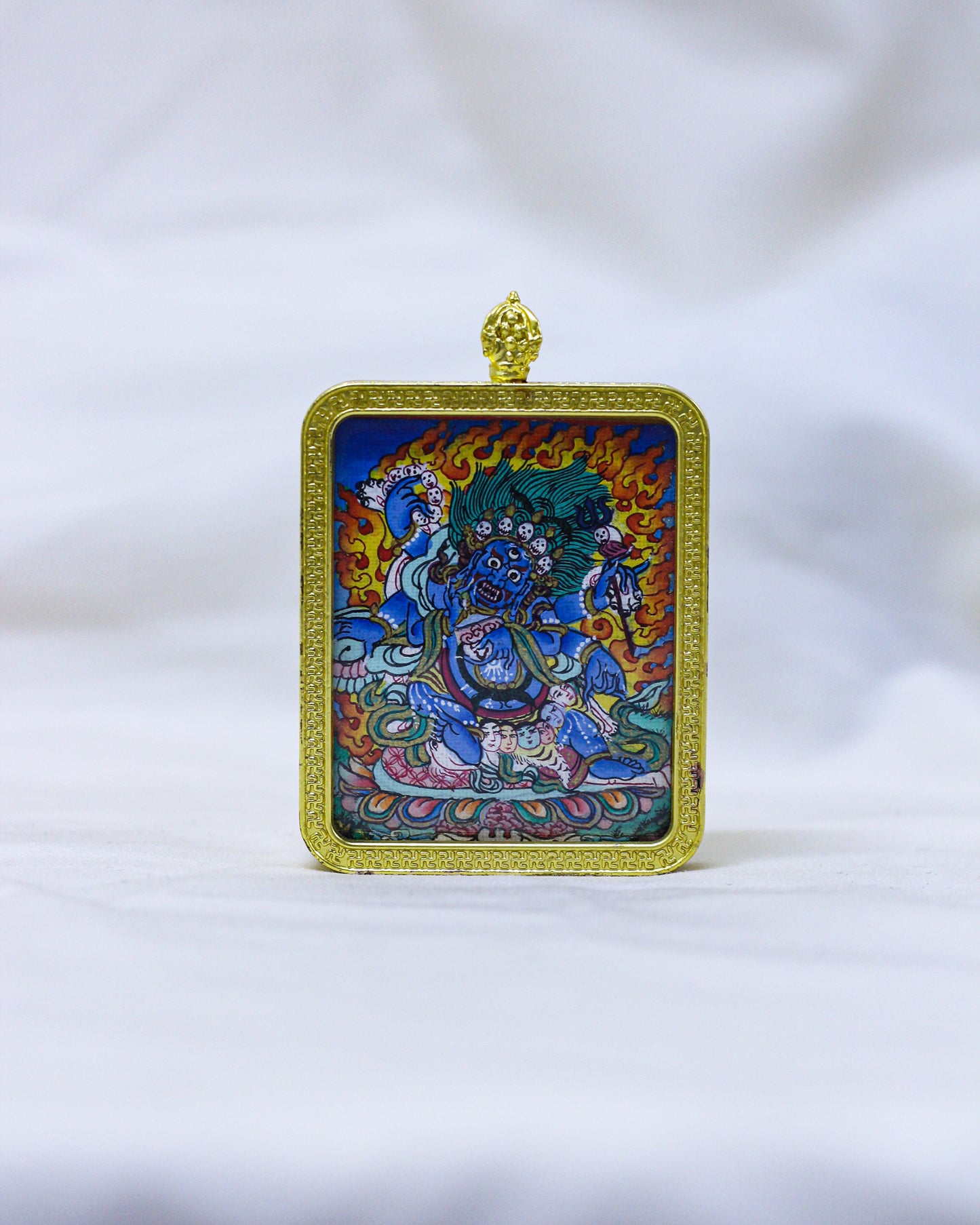 A Tibetan Buddhist Mahakala Thangka Pendant Necklace framed in ornate gold metal with a hanging loop of vajra at the top