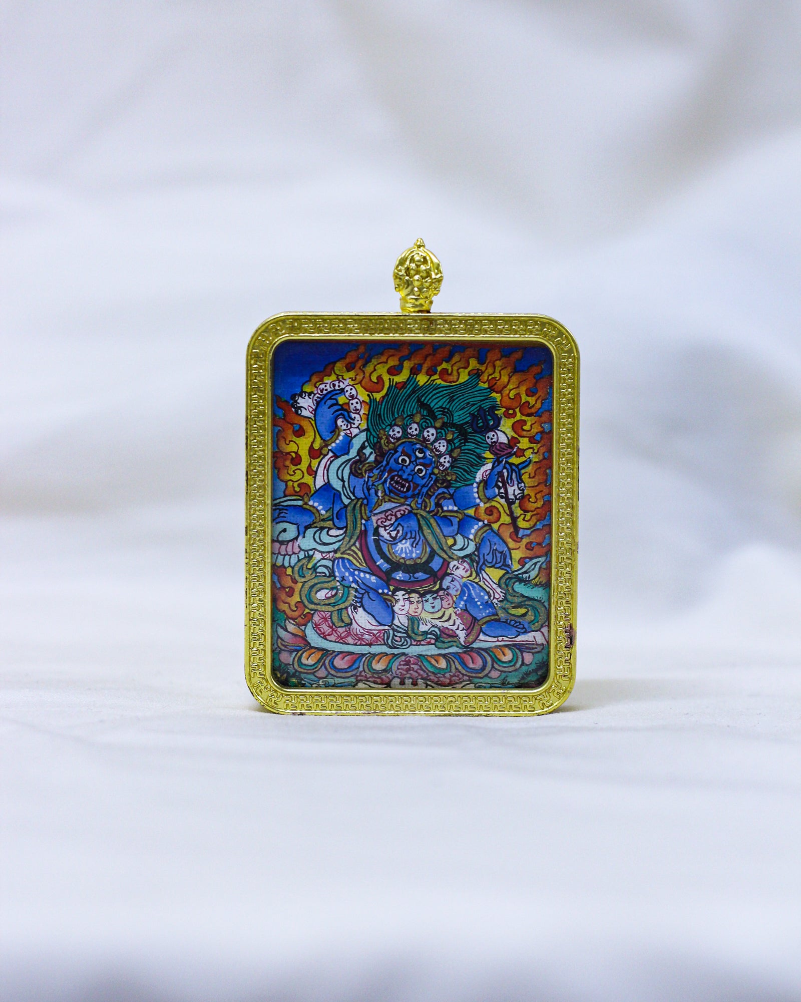 A Tibetan Buddhist Mahakala Thangka Pendant Necklace framed in ornate gold metal with a hanging loop of vajra at the top