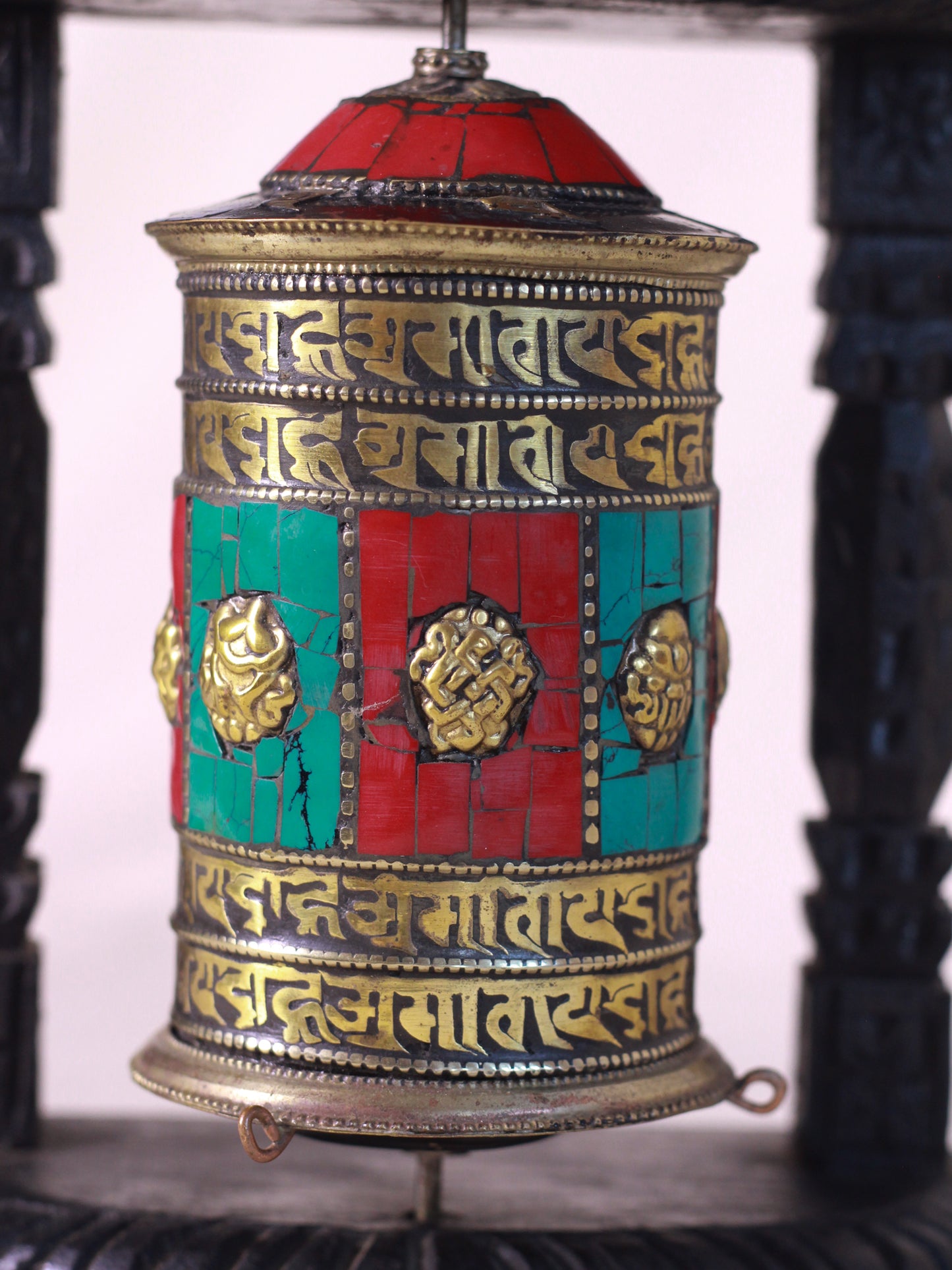 Close-up view of a handcrafted  Buddhist prayer wheel with carved wooden frame and red turquoise decorative inlay